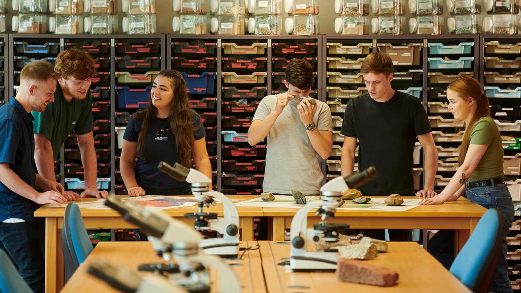 A group of students work in the geology lab, using geological maps and rock specimens, and discuss their work.