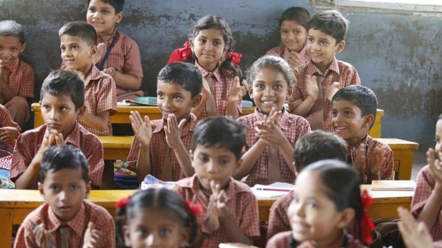 Young children wearing school uniform sitting in rows looking happy and clapping