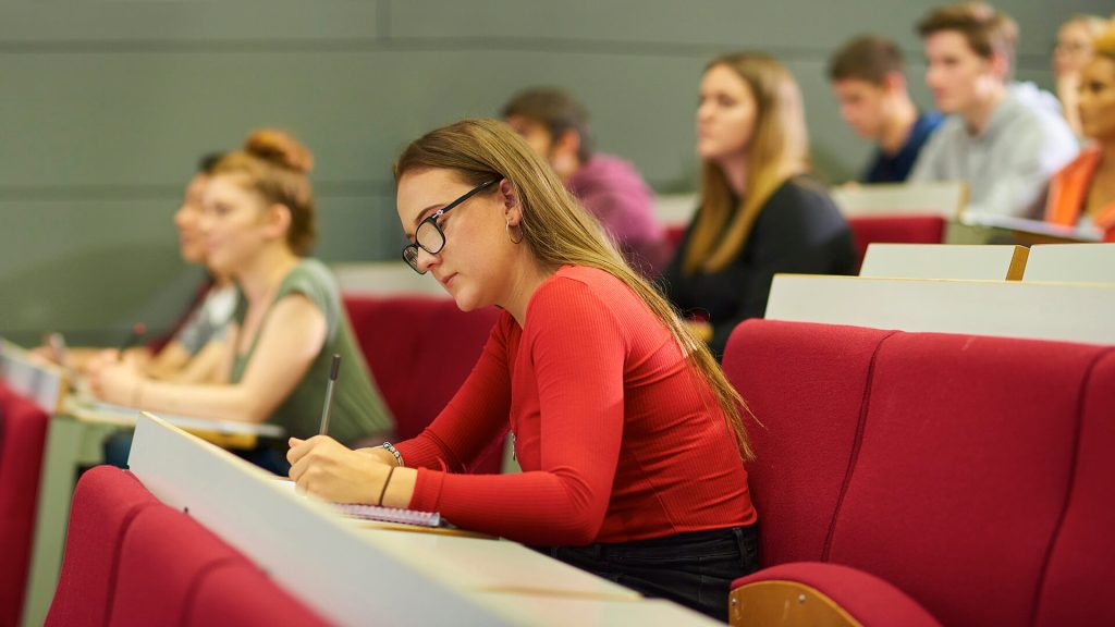 A student sat making notes in a lecture theatre.