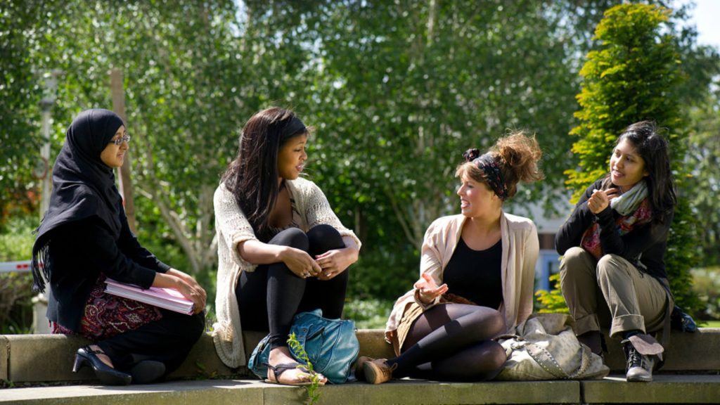 Four students talk, sitting on the grass on campus