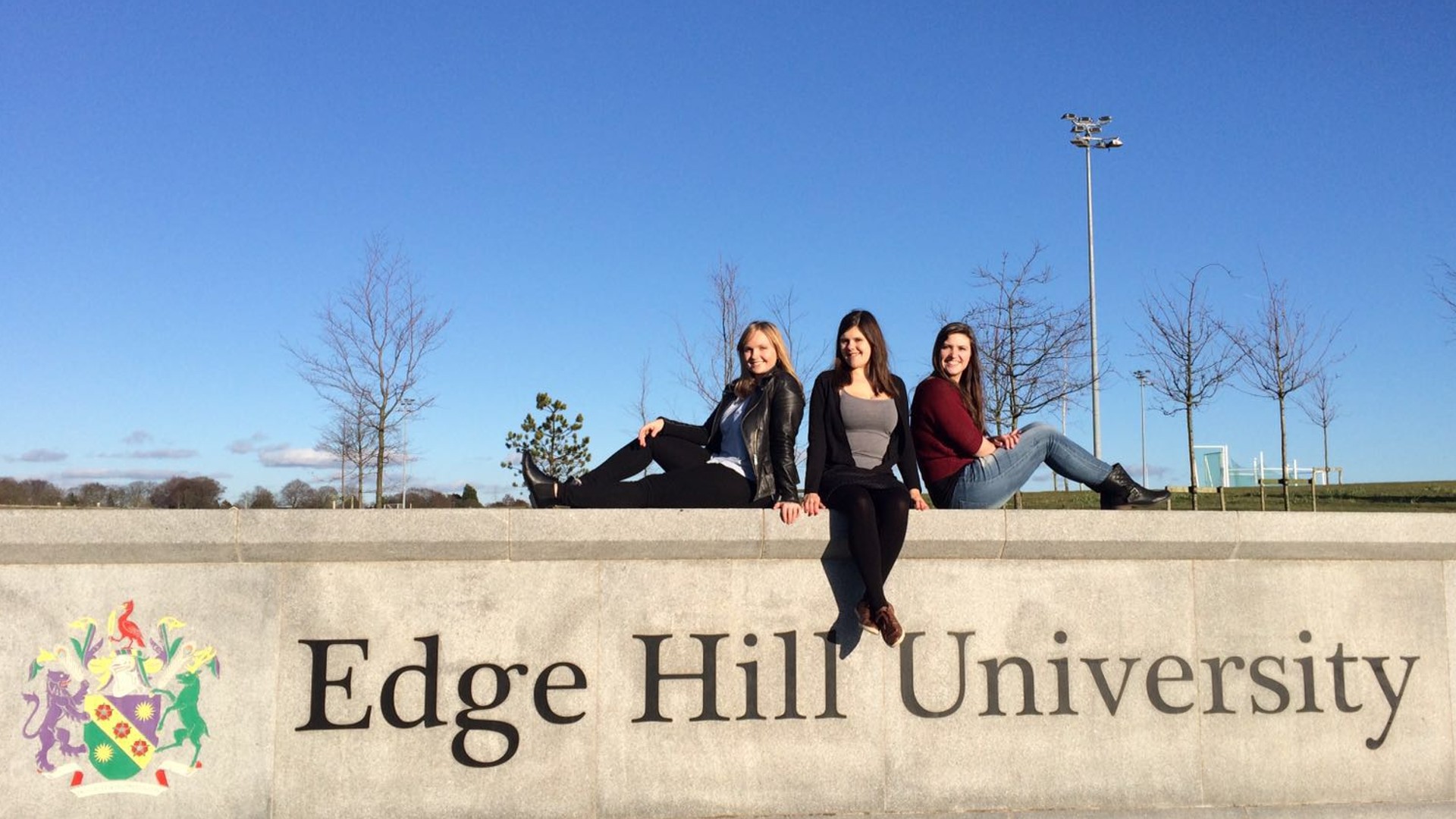 Three students sat on the Edge Hill University sign