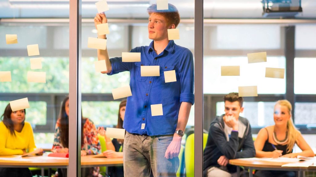 A student places post-it notes on a glass window during a seminar.