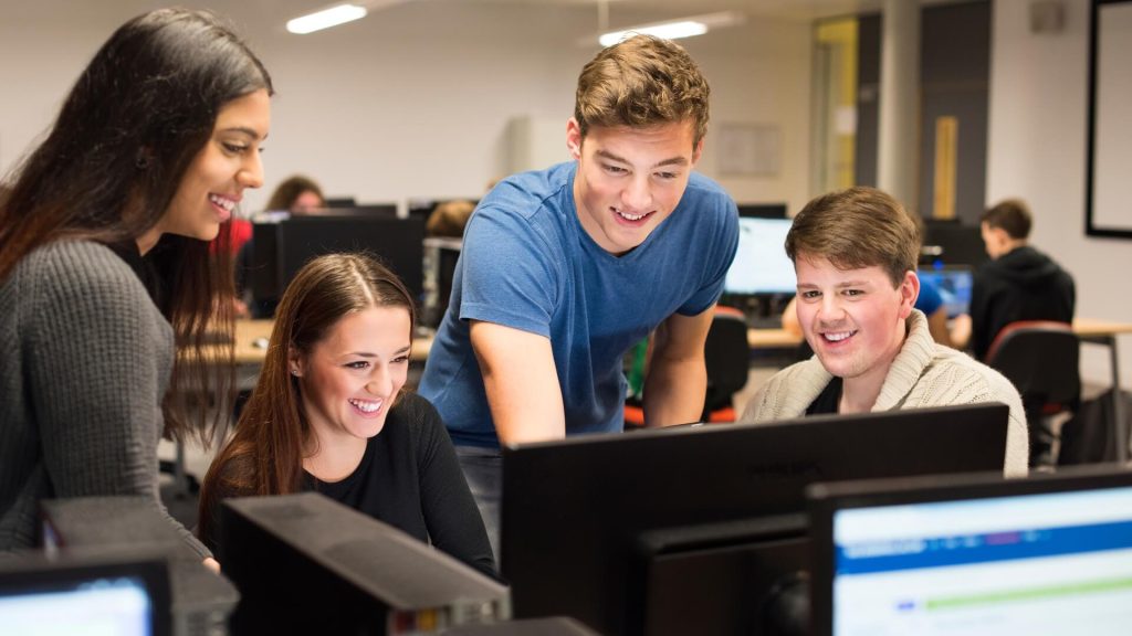Students gather round a computer screen in a computer lab.