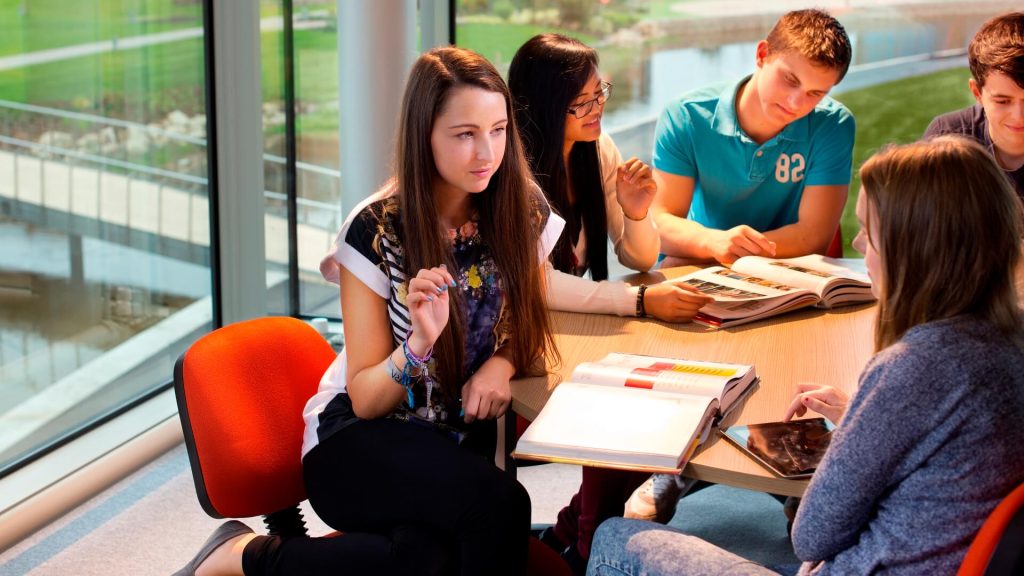 Five students study textbooks while working together in a room in Creative Edge overlooking the lake on the eastern side of campus.