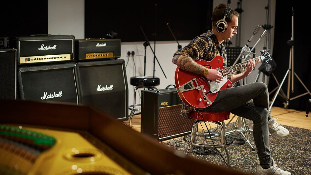 A student plays the guitar in a music studio.