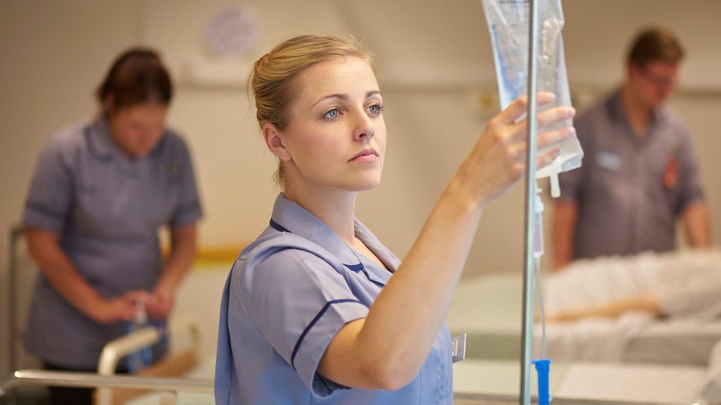 A student nursing associate examines a drip while using the clinical skills facilities.