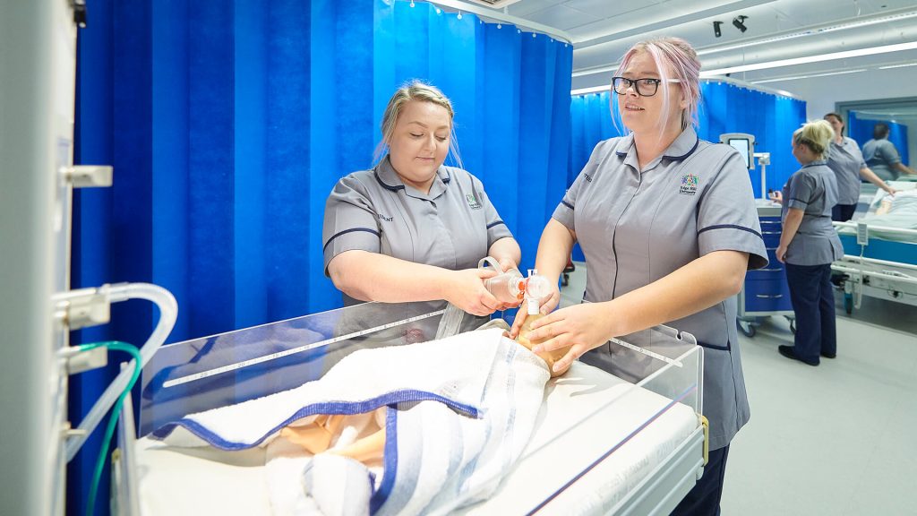 Two student nurses monitor a child manikin in a simulated clinical skills setting.
