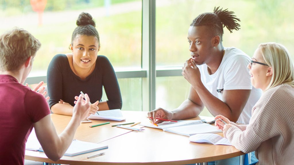 Four students sat around a table engaging in discussion and taking notes.