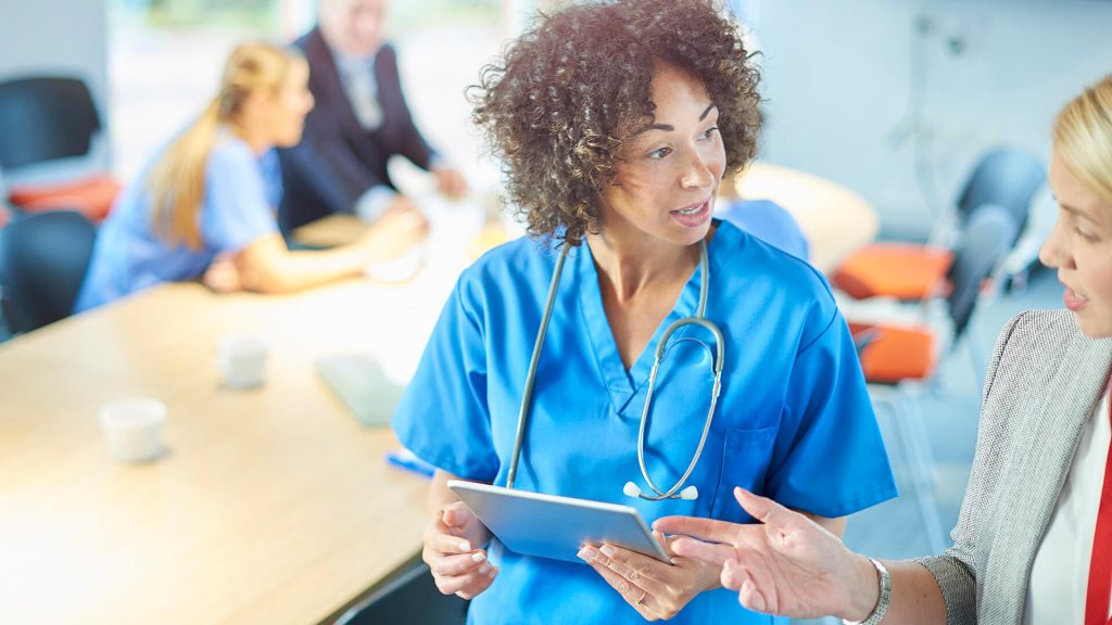 A nurse with stethoscope speaks with a colleague.