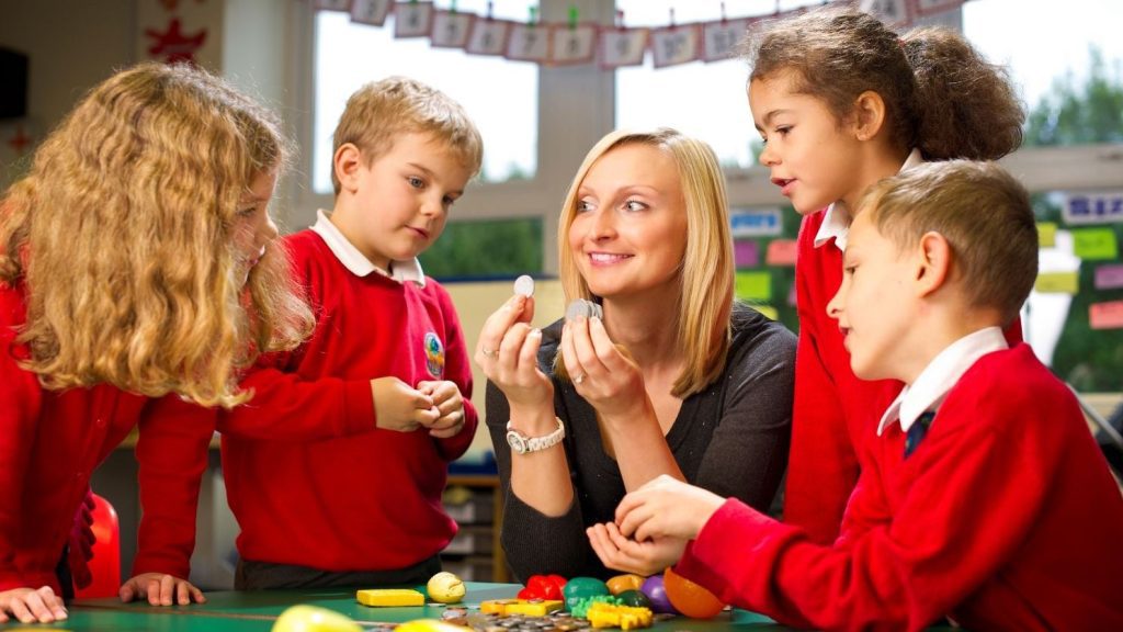 A primary teacher counts coins with pupils in a school classroom.