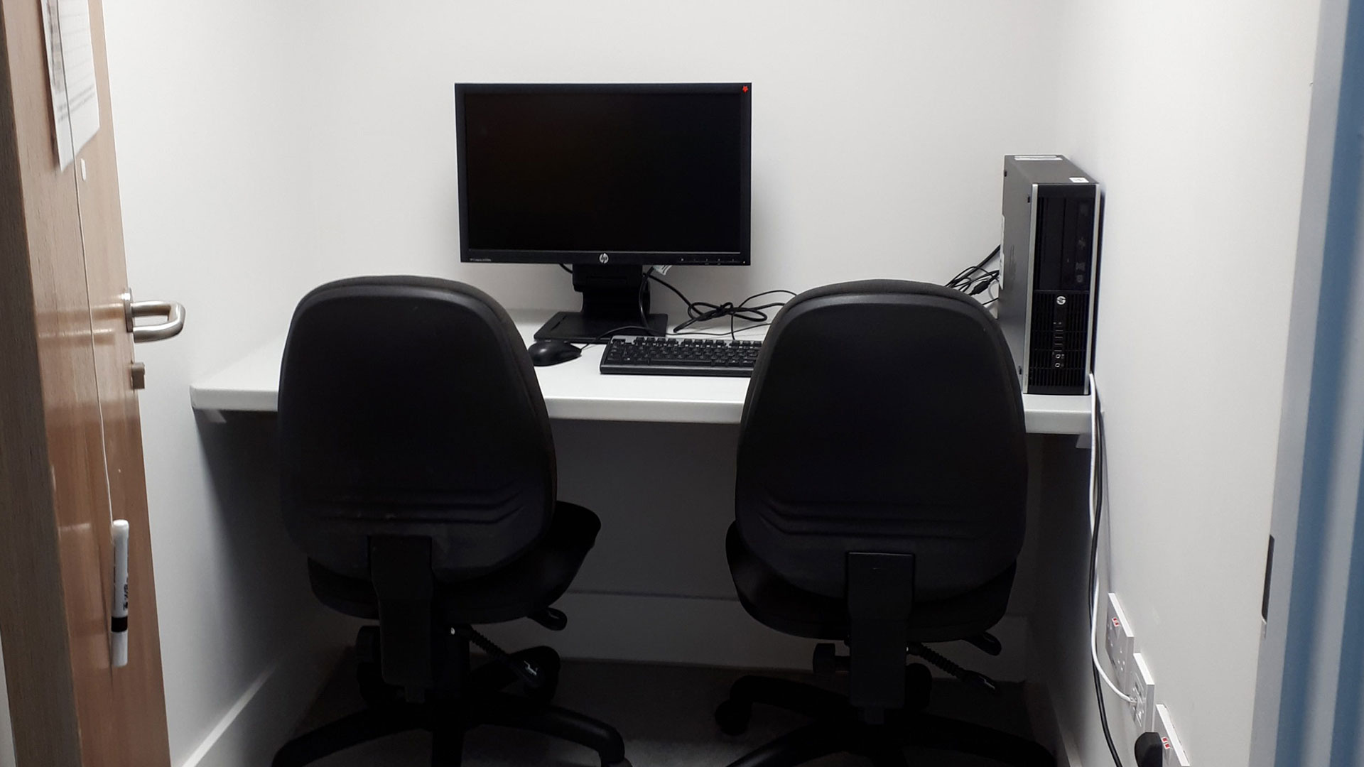 A small cubicle room with a computer and two chairs in the Psychology building