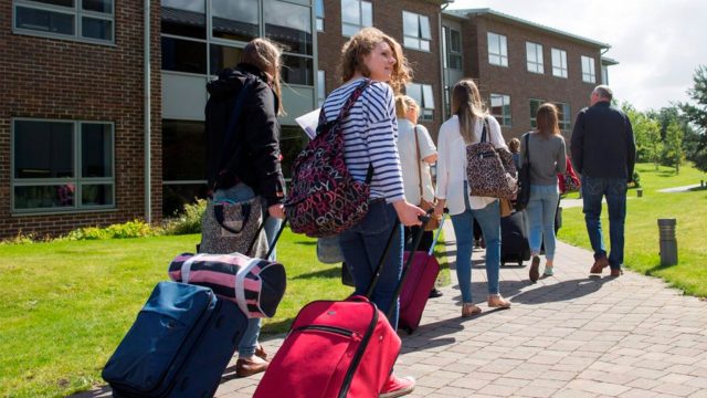 Students with suitcases walking towards a halls of residence