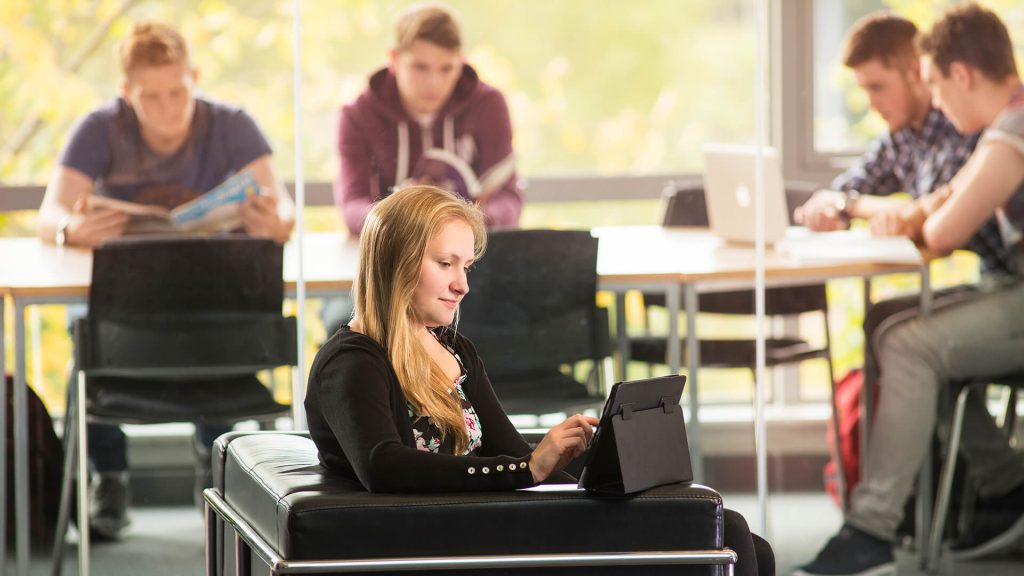 A student uses a tablet while sat on a sofa in Creative Edge.