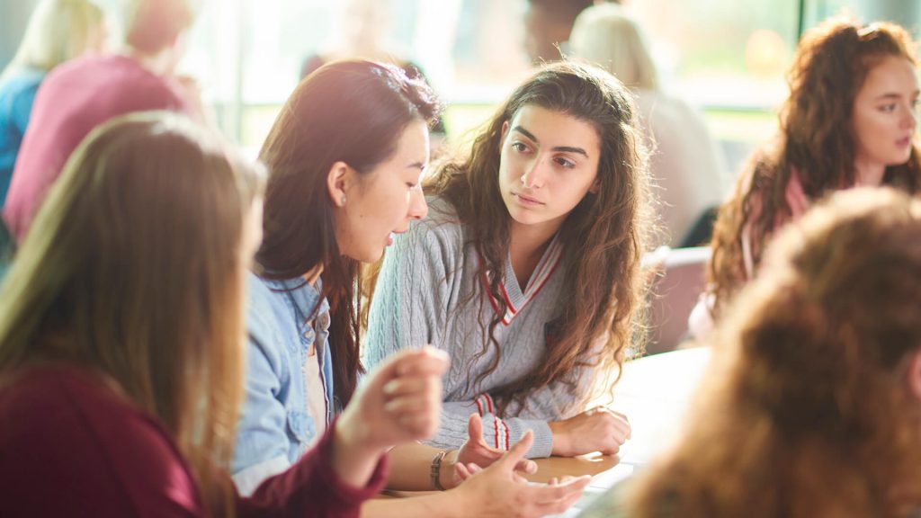 Students sit behind a desk and engage in a group discussion during a seminar in the Faculty of Health, Social Care and Medicine.