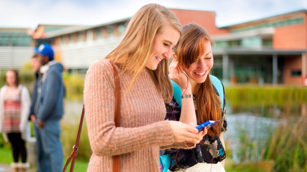 Two students walking past a lake to the western side of the campus, with the Faculty of Education building in the background.