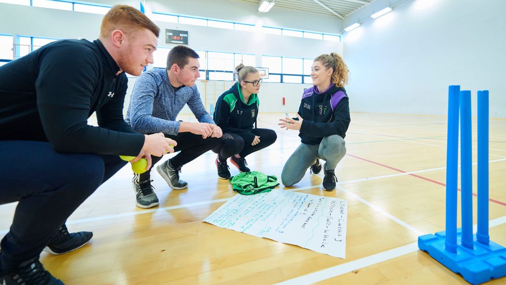 Sports students in the gym, with notes on paper on the floor.