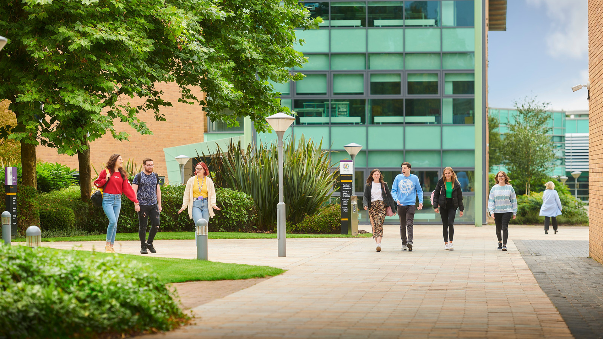 Two groups of students walking through campus. The Clinical Skills and Simulation Centre, and Faculty of Health, Social Care and Medicine buildings are in the background