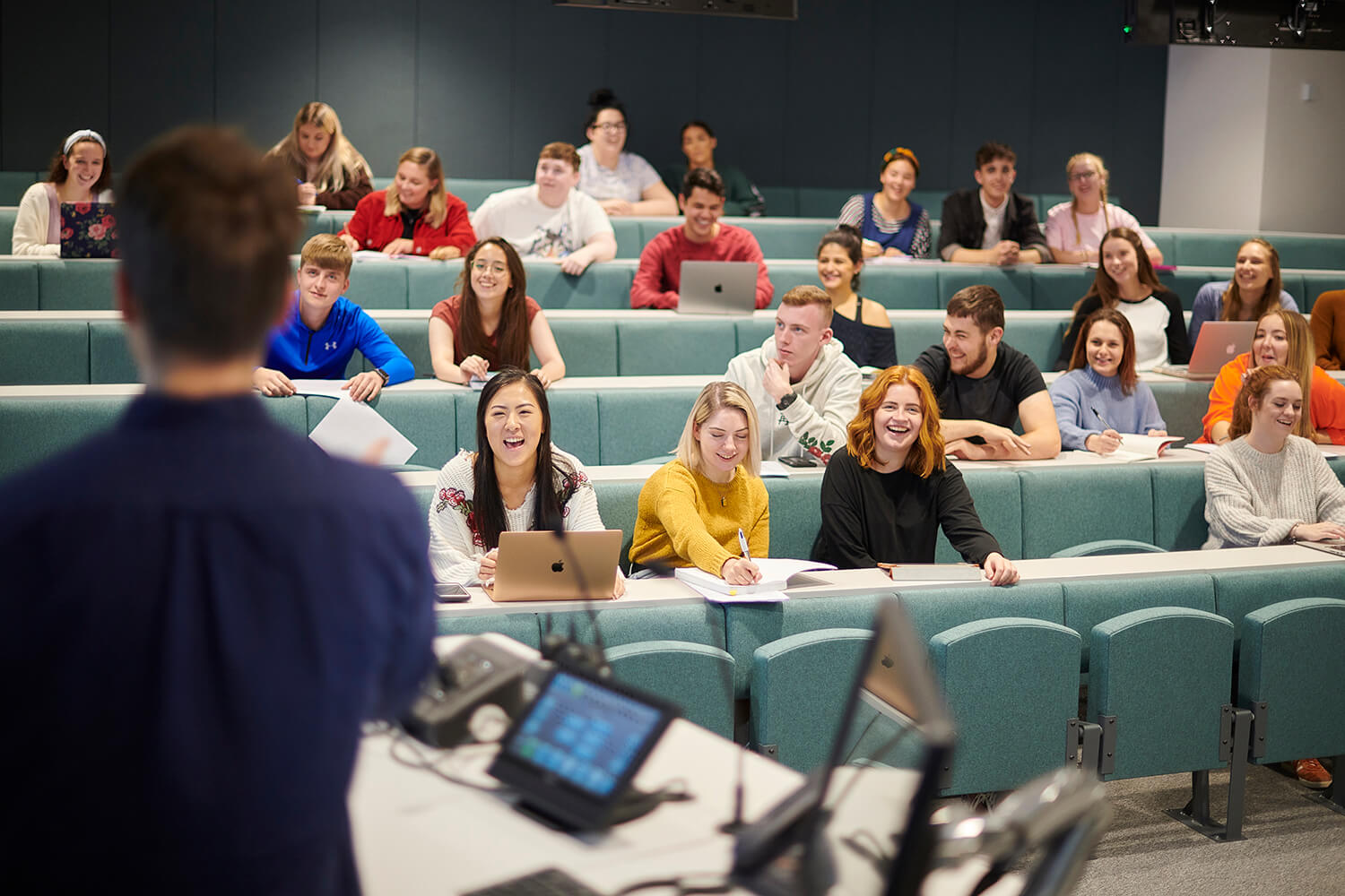A lecturer addresses a class of students in a Harvard-style lecture theatre.