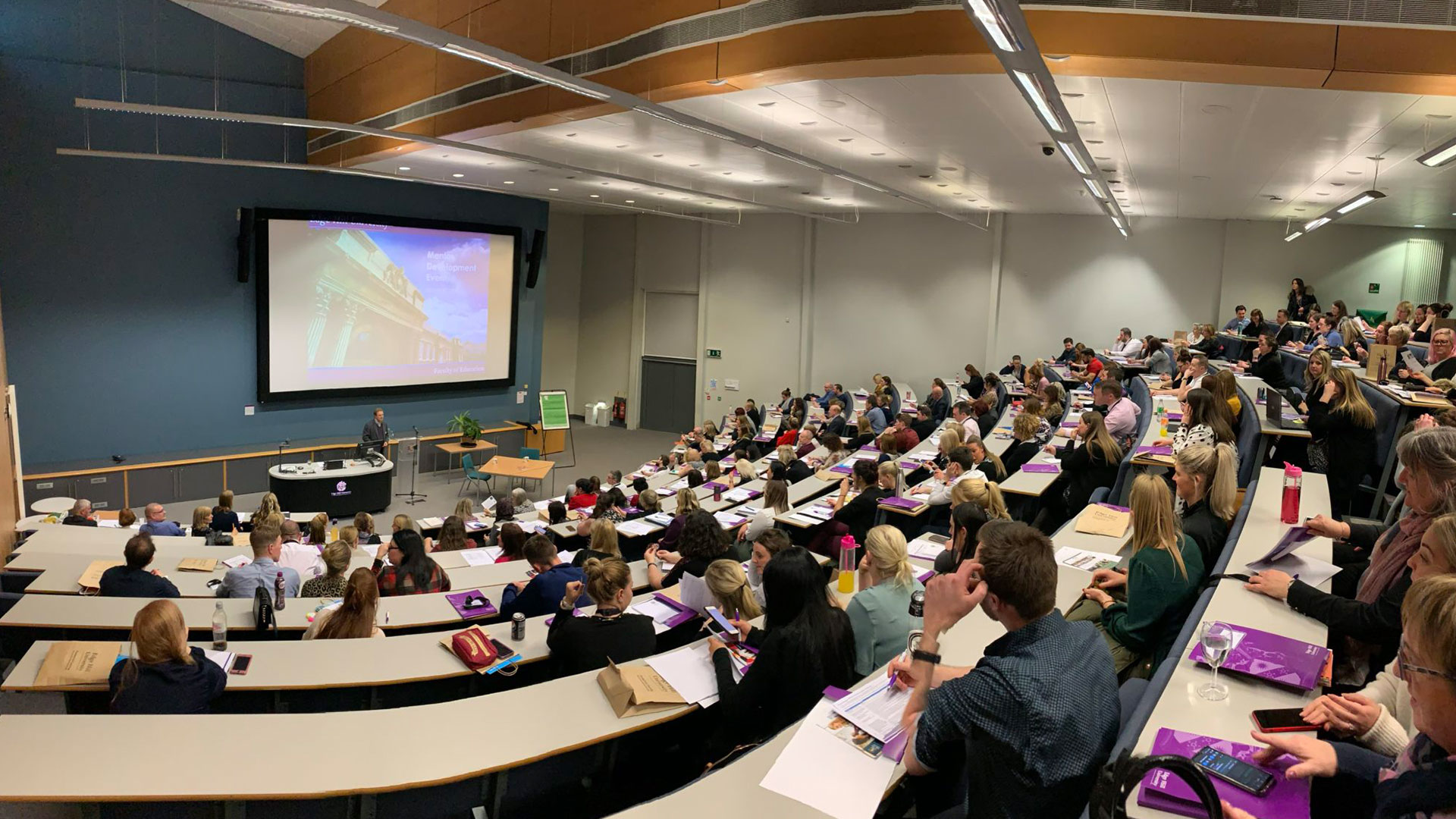 A lecture theatre full of people, with someone giving a presentation at the front