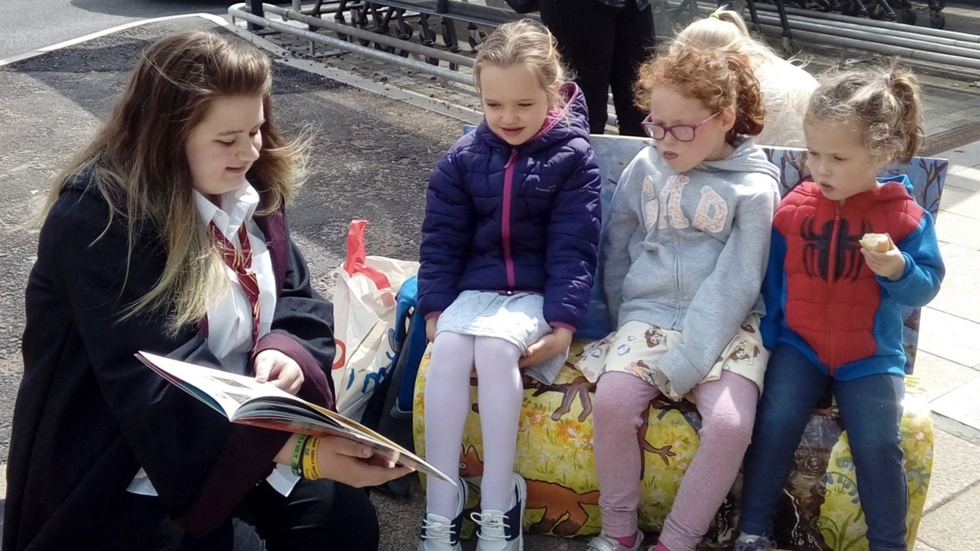 Children-sitting-on-a-decorated-bench-listening-to-someone-reading-a-story