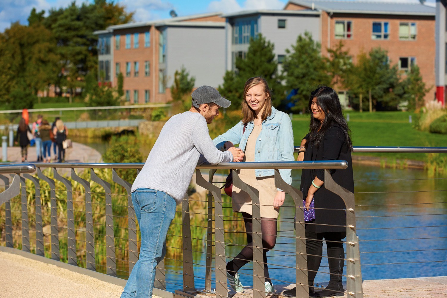 Three students talk by a bridge over the lake by Chancellors Court and Chancellors South.