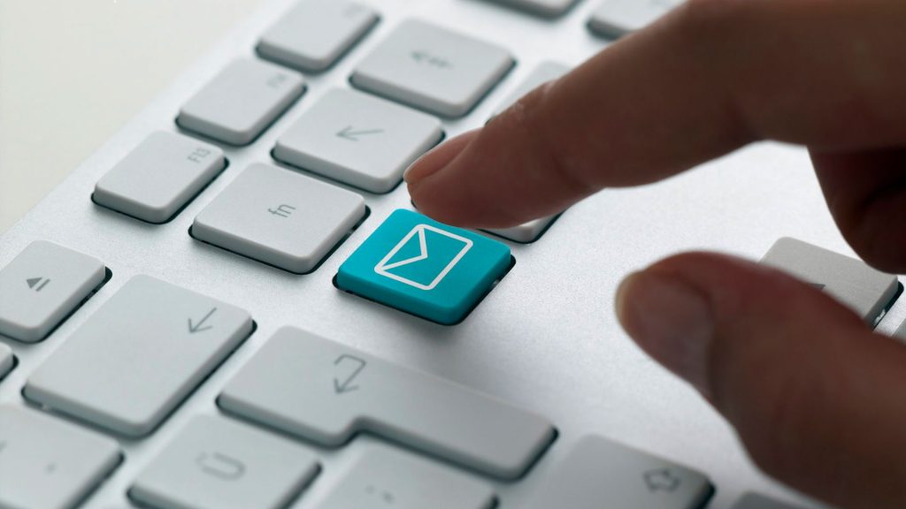 A persons hand hovering over an email key on a computer keyboard