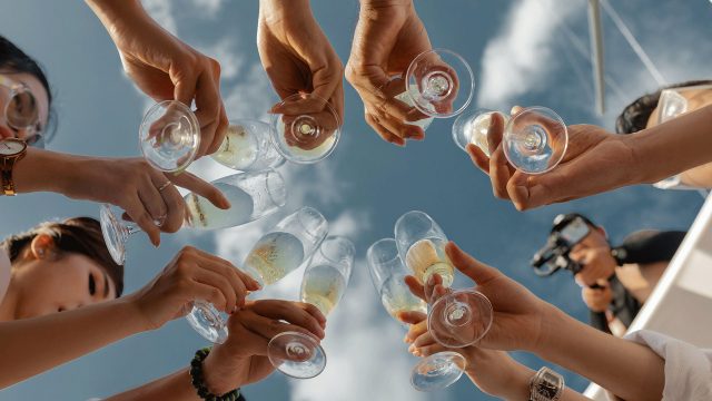 Group of people holding champage glasses up, with a blue sky above them