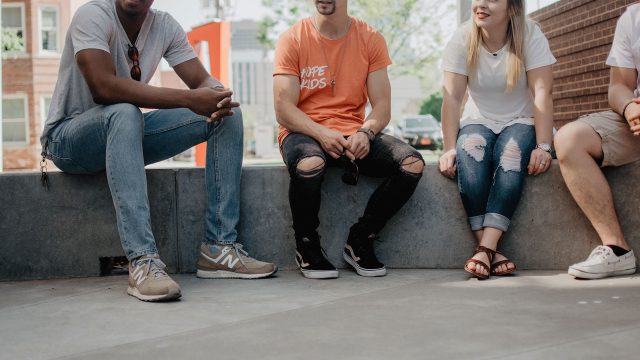 A group of unrecognisable people sitting on a concrete step talking together