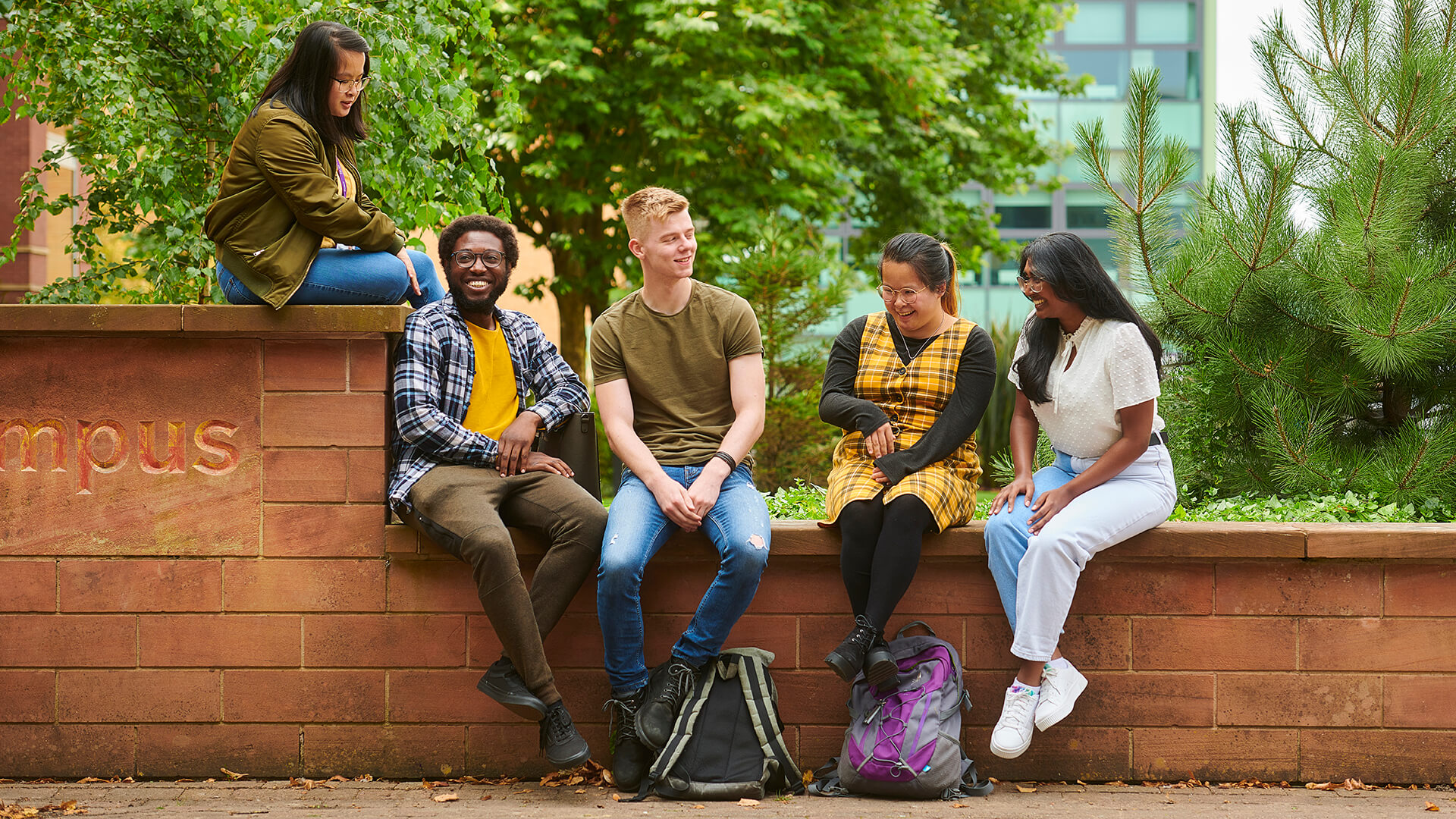 Five students chat while sat by the piazza on campus, with the Clinical Skills and Simulation Centre visible behind them.