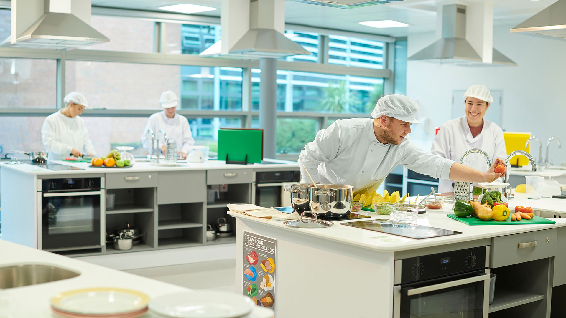 Students in the Nutrition labs in the Faculty of Health, Social Care and Medicine. They are wearing their lab clothing and working with food.