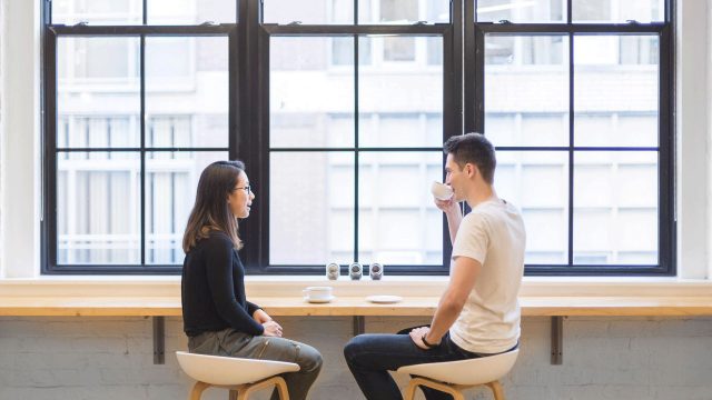 Two people in front of a huge window drinking coffee
