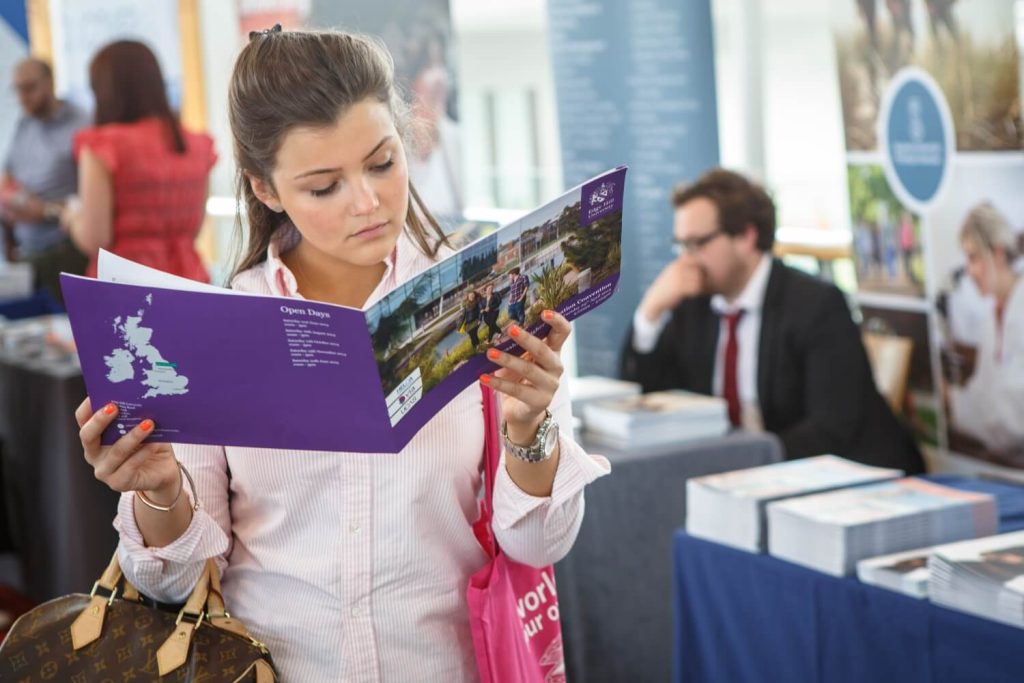 A young woman reading a purple booklet at a UCAS fair