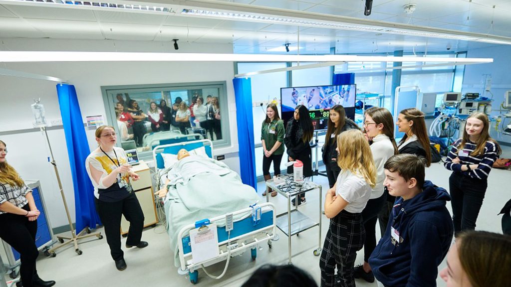 An open event in the Clinical Skills and Simulation Centre. There are prospective healthcare students participating in a simulation practice, being instructed by a professional.