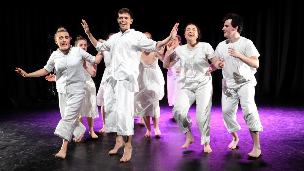 A group of performers on stage dressed all in white