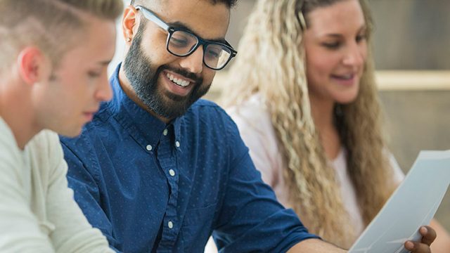 Students smile and talk while looking at work on a piece of paper