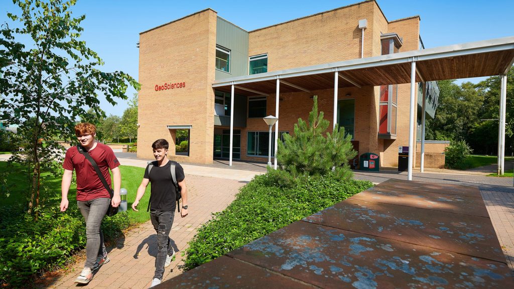 The outside of the Geosciences building with two students walking