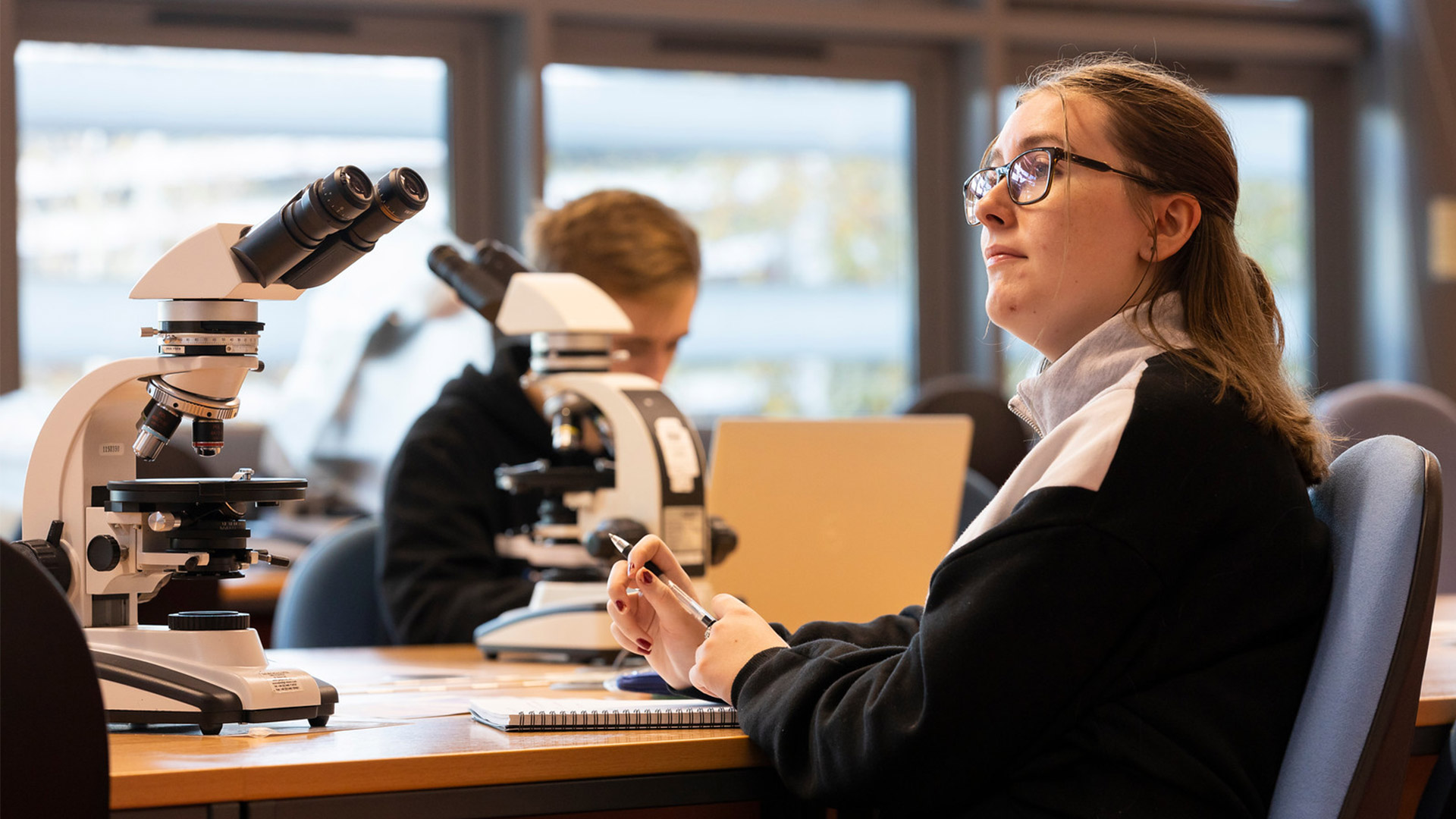 Geography student using microscopes and referencing a map in the lab