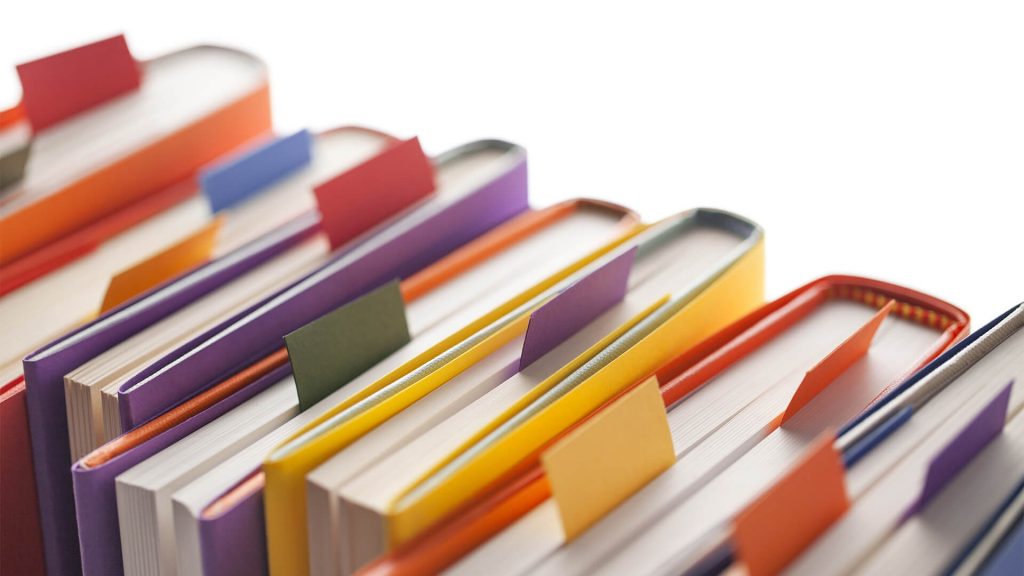 There are various coloured books, each have a different coloured tab coming out of the top of the book. The background of the image is white.