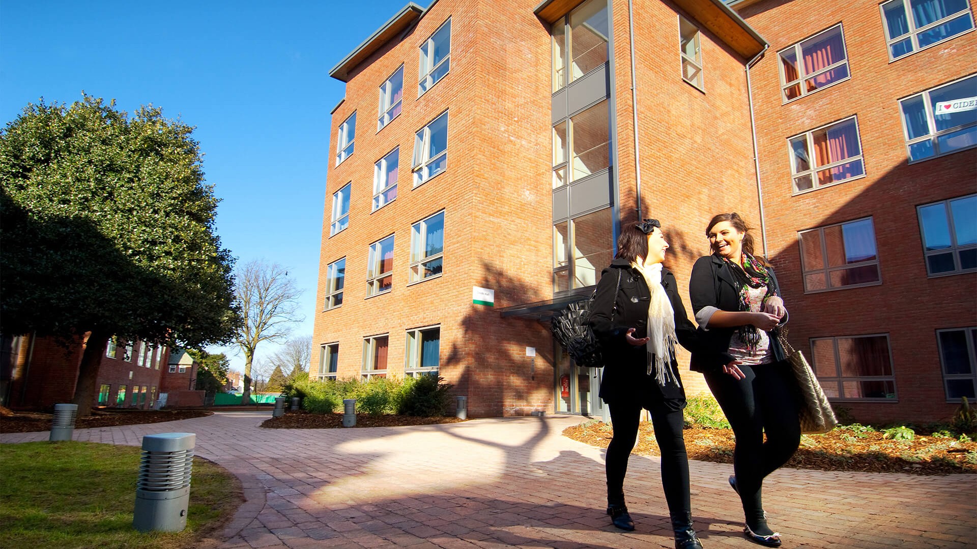 An image of two people walking past one of the accomodation blocks at Edge Hill University. The image is set in the day.