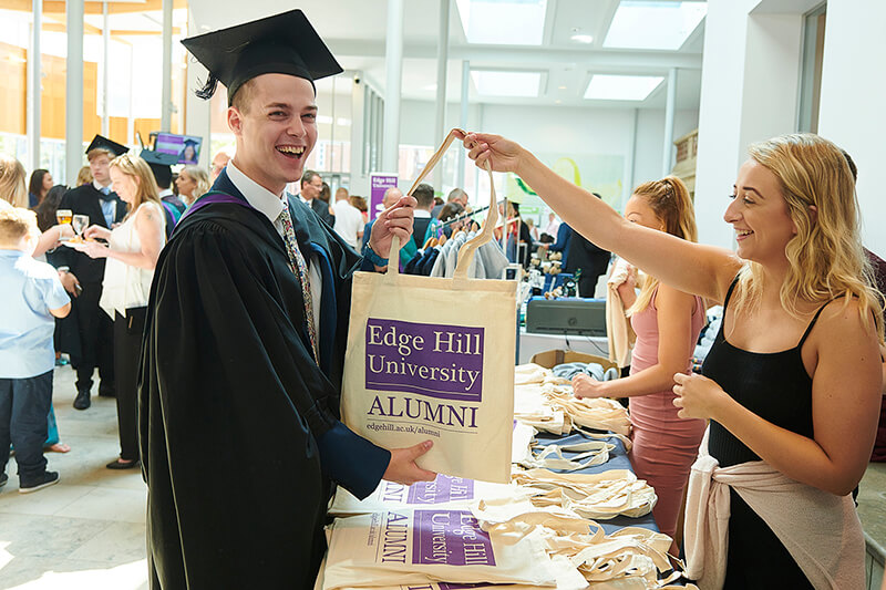 A graduate picks up an alumni bag from a stall in the Hub.