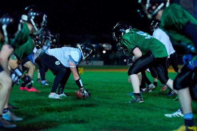 Students wearing helmets compete in a game of American football.