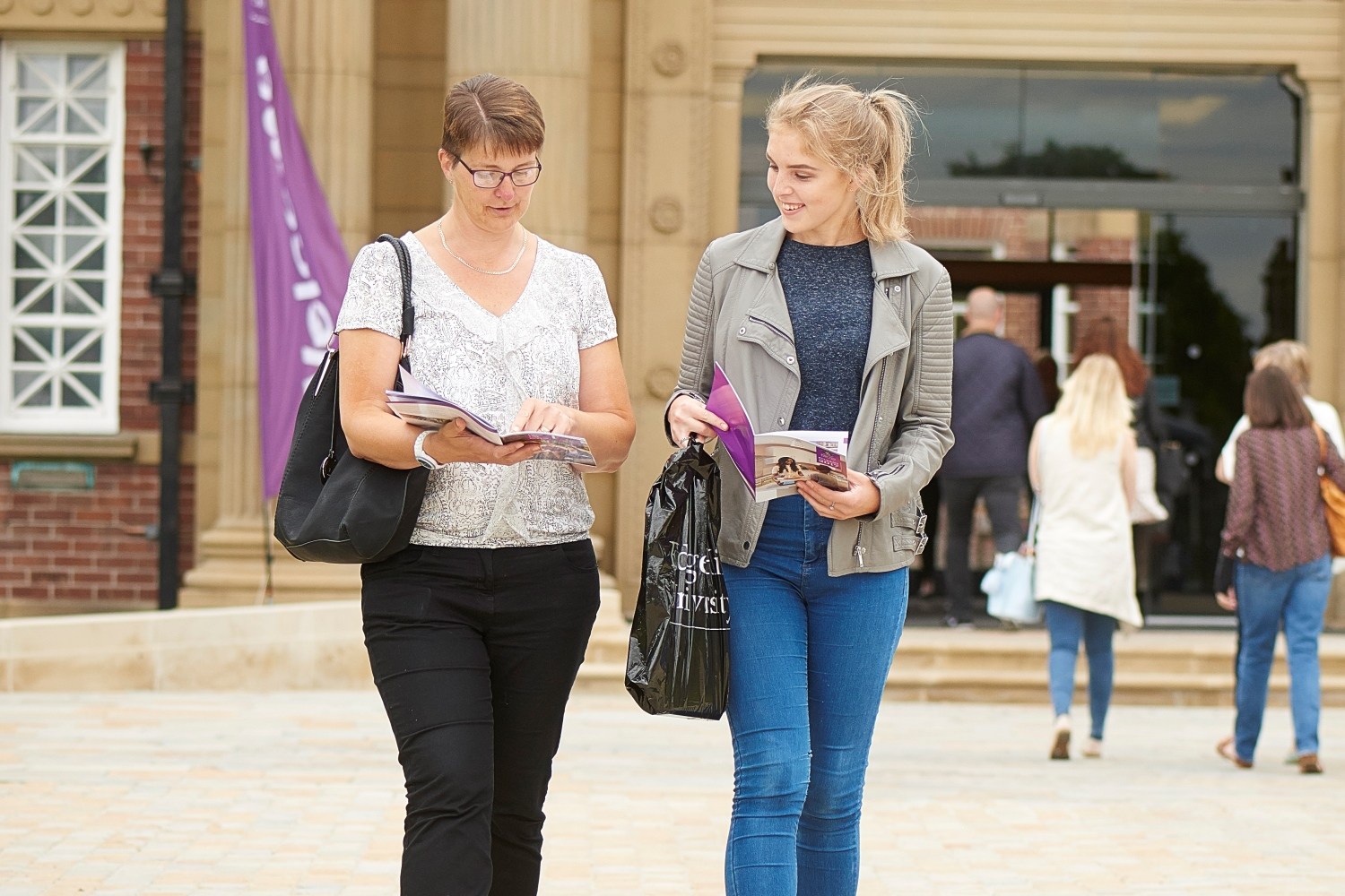 A student and their mum consult a printed open day guide while walking near the Main Building during an open day.
