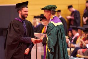 A graduate shakes the hand of Dr John Cater as he receives his award.