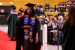 A graduand walks along the red carpet after shaking the hand of Dr John Cater during a graduation ceremony.