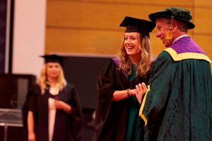 A graduate poses for a photo while shaking Dr John Cater's hand during a graduation ceremony.