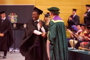 A graduate walks along the red carpet after receiving his degree from Dr John Cater.