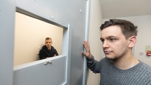 One student sat in the mock prison cell and another student looking in the cell from outside.