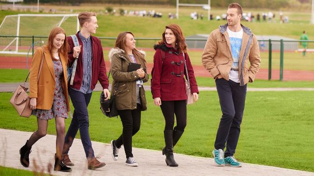 An image of five people walking along a path on the Edge Hill University campus. 