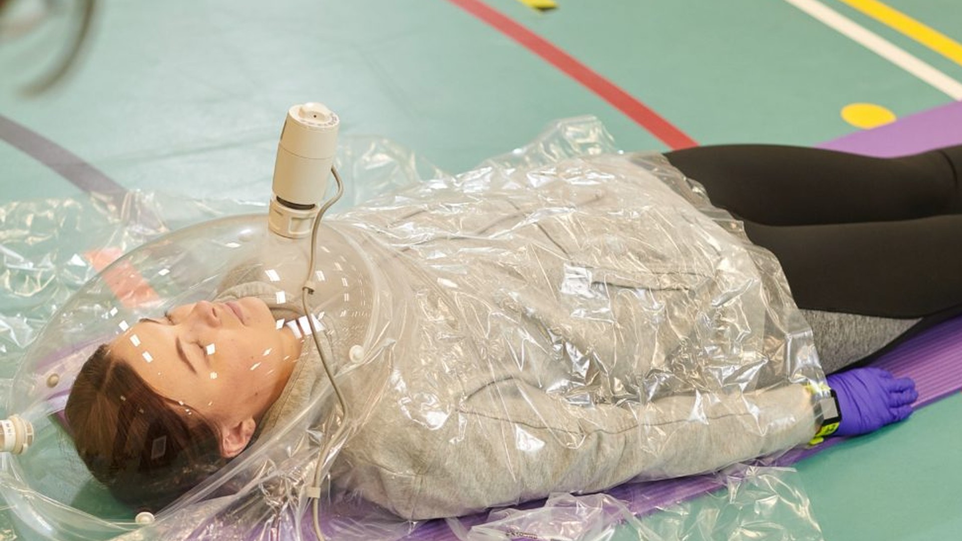 An image of a person lay on the floor with a large see-through mask over their head.
