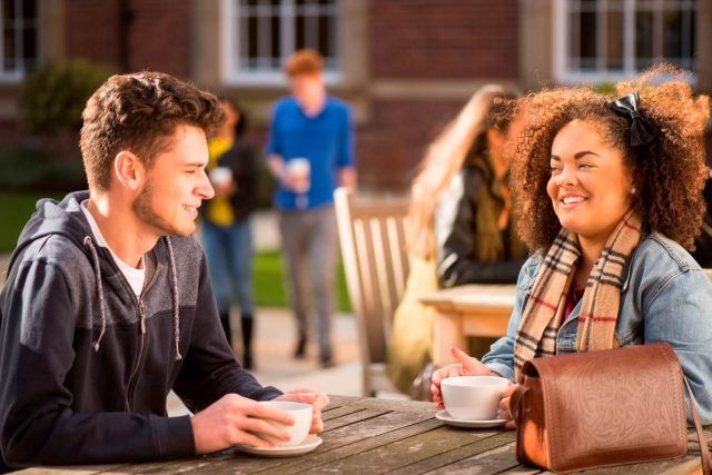 Two students enjoy a coffee outdoors in the Quad by the Main Building.